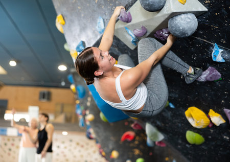 Confident young woman scaling artificial climbing wall in climbing gym