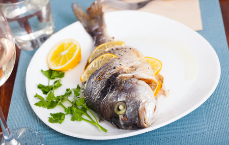 Delicious grilled gilthead bream (dorada) with lemon served at plate with greensの写真素材