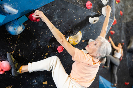 Confident mature woman scaling artificial climbing wall in climbing gymの写真素材
