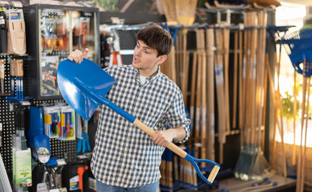 Guy in hardware store examines shovel and spade.の写真素材