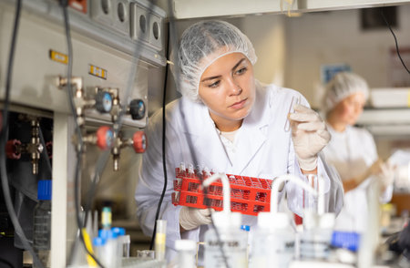 Female scientist researcher looking at reaction in test tube while performing biochemical tests in...