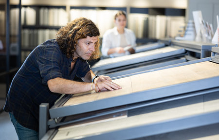 in hardware store, buyer carefully examines laminate sample. Man chooses flooring materialの写真素材