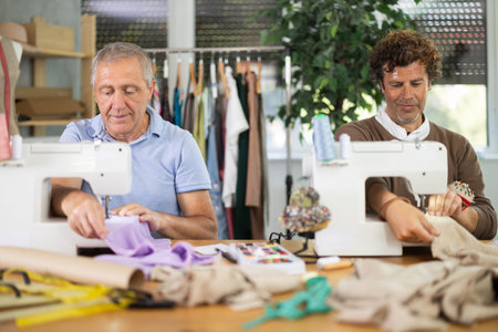 Two tailors sitting in a sewing workshop and working