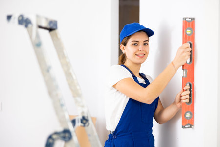 Woman builder using building level measures the vertical of wall