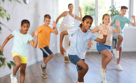 African boy dances vogue in choreographic school, friends and teacher dance in gym blurry background