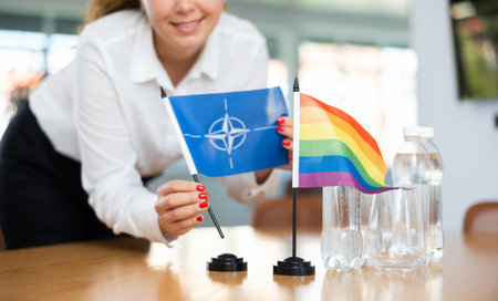 Young woman puts NATO and LGBT flags on table in officeのeditorial素材