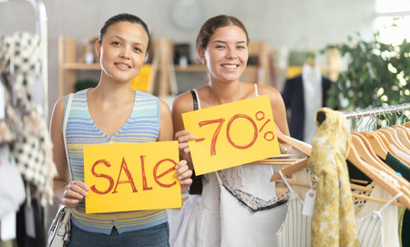Two happy women holding a sign saying Sale in the interior of fashion store