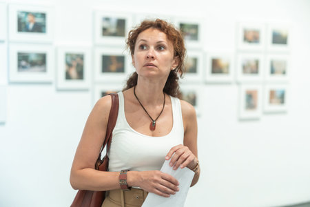 Middle-aged woman looking at pictures on wall in museum