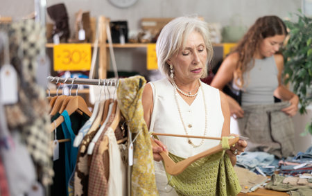 Attentive mature woman choosing something for summer in clothing storeの写真素材