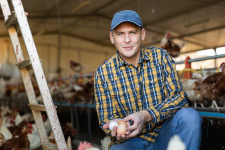 Successful poultry farm owner standing with eggs in hands in henhouseの写真素材