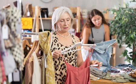 Attentive mature woman choosing something for summer in clothing store