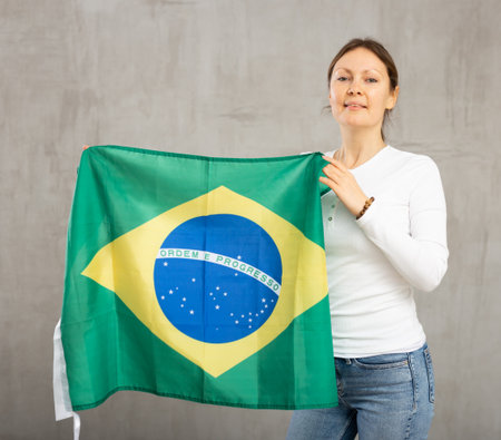Portrait of confident calm smiling female standing against gray wall with national flag of Brazilの写真素材