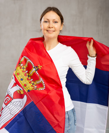 Smiling relaxed woman with national flag of Serbia against gray wall backgroundの写真素材