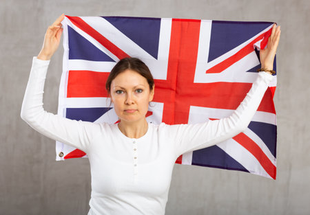 Sad young woman holding flag of Great Britain against unicoloured backgroundの写真素材
