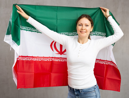 Portrait of confident calm smiling female standing against gray wall with national flag of Iranの写真素材