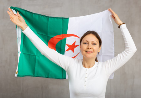 Happy young woman holding flag of Algeria against unicoloured backgroundの写真素材