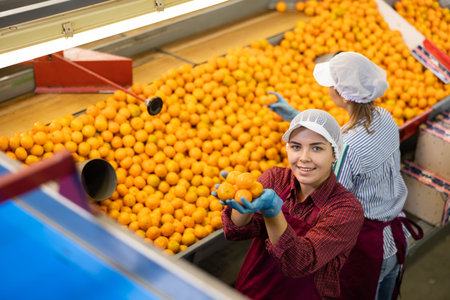 Happy young female worker of sorting line holding tangerines