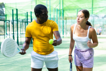 Portrait of concentrated african american trainer teaching woman playing padel outdoorの写真素材