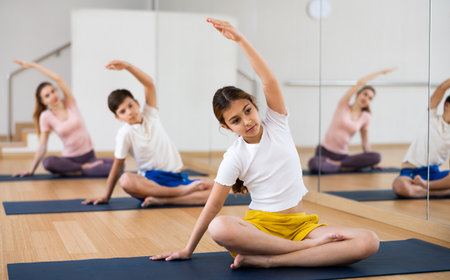 Girl doing stretching in Padmasana pose with brother and parents in yoga studioの写真素材