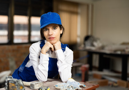 Positive woman repairer in uniform standing inside apartment and looking at cameraの写真素材
