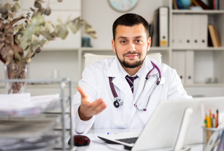 Cheerful man physician sitting at desk and explaining with gestureの写真素材
