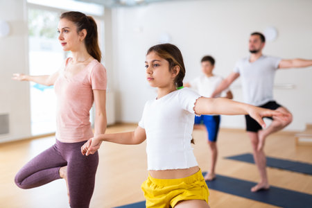 Young girl standing in tree pose with her mother during yoga trainingの写真素材