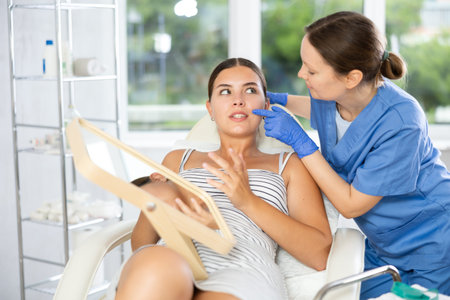 Adult female cosmetologist examining face of female patient