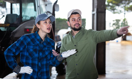 Man and woman farmers standing at tractor and talkingの写真素材