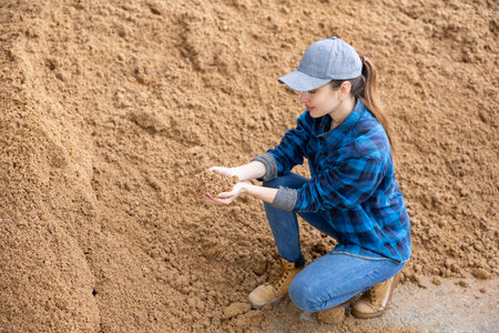 Female farmer checking quality of beer bagasse in storage area outdoors