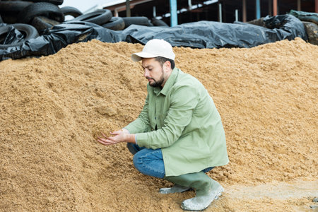 Farmer squatting at large heap of brewers spent grainの写真素材