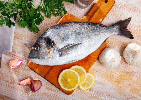 Uncooked whole dorado fish with lemon, garlic and greens