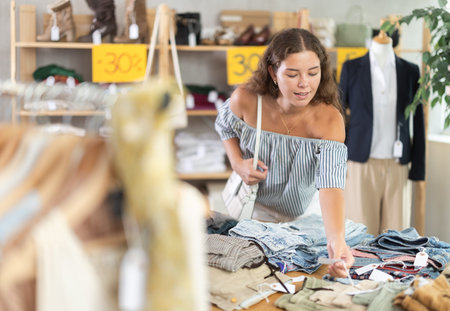 Young woman choosing trousers in clothing store