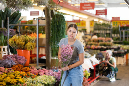 Young woman customer choosing bundle of limonium in open-air plants market