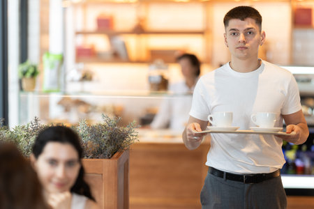 Young man with coffee walking to table in cafe
