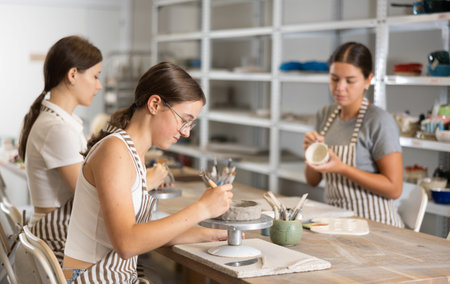 Woman teacher and students sculpt and paint ceramics