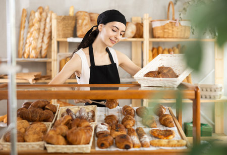 Young woman seller puts croissants in showcase