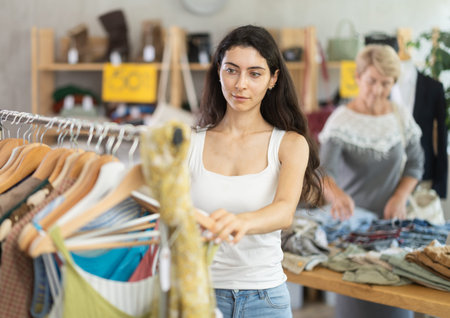 Young woman customer elect something summer clothes in store. Female client choosing something in...