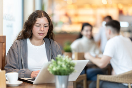 In cozy cafe hall, freelance girl works with laptop and drinks coffee.