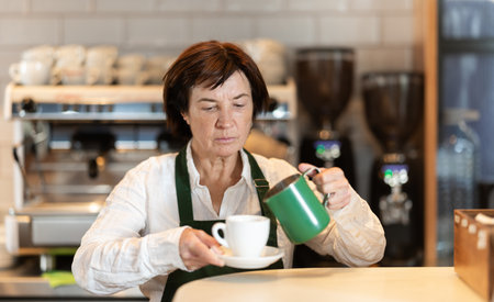 Elderly woman barista pouring coffee in cafeの写真素材