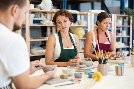 Three pottery workshop workers sculpt from raw clay