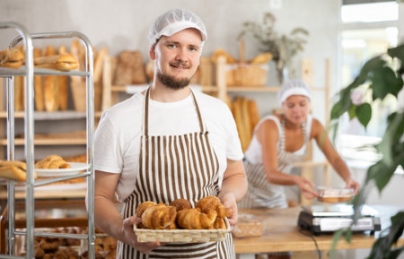 Male seller holds basket with finished products, shows many croissantsの写真素材