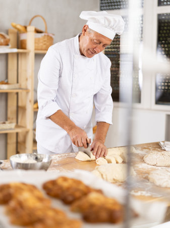 Experienced aged baker portioning dough on floured table