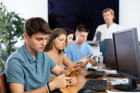 Focused young student using smartphone while studying in computer workshop