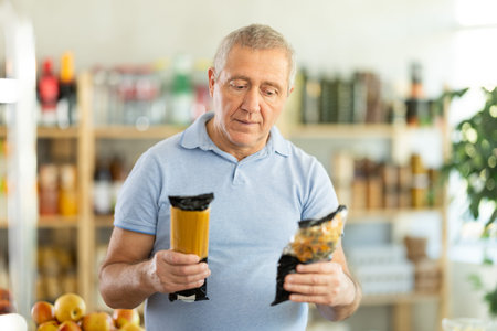 Mature man choosing package of pasta in grocery storeの写真素材