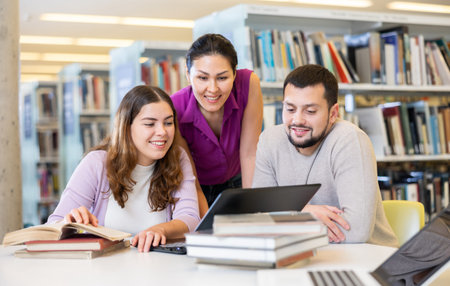 Three adult students work on laptop and read books in a public library