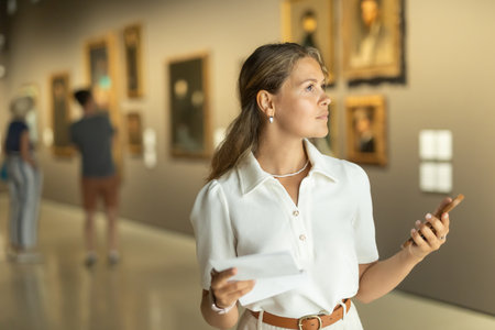 Portrait of young girl visitor with paper guide at the exhibition of paintings in museumのeditorial素材