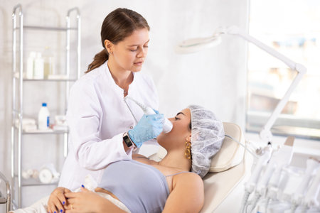 Brunette girl having facial beauty procedure with ice hummer