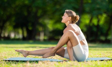 Girl in park on green grass of lawn performs Chakorasana
