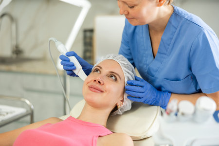 Professional cosmetologist doing ultrasonic facial cleansing for young woman in spa center....