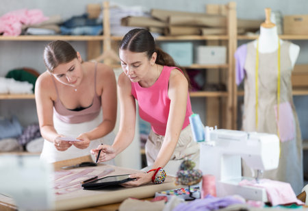Adult and young seamstresses drawing pattern on tablet